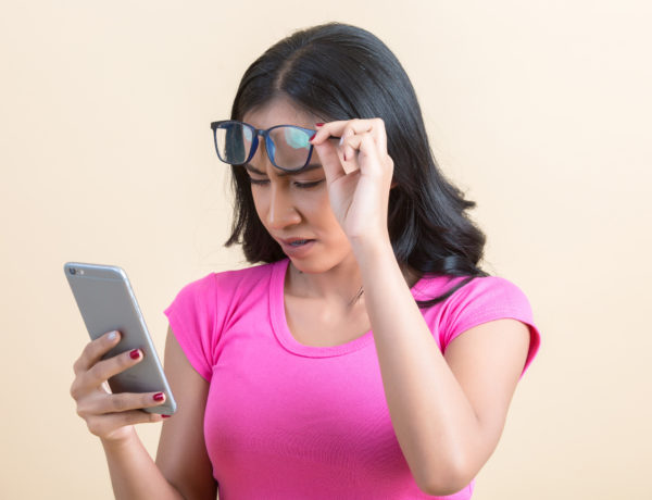 chica con miopía por pantallas levantando sus gafas para mirar un movil